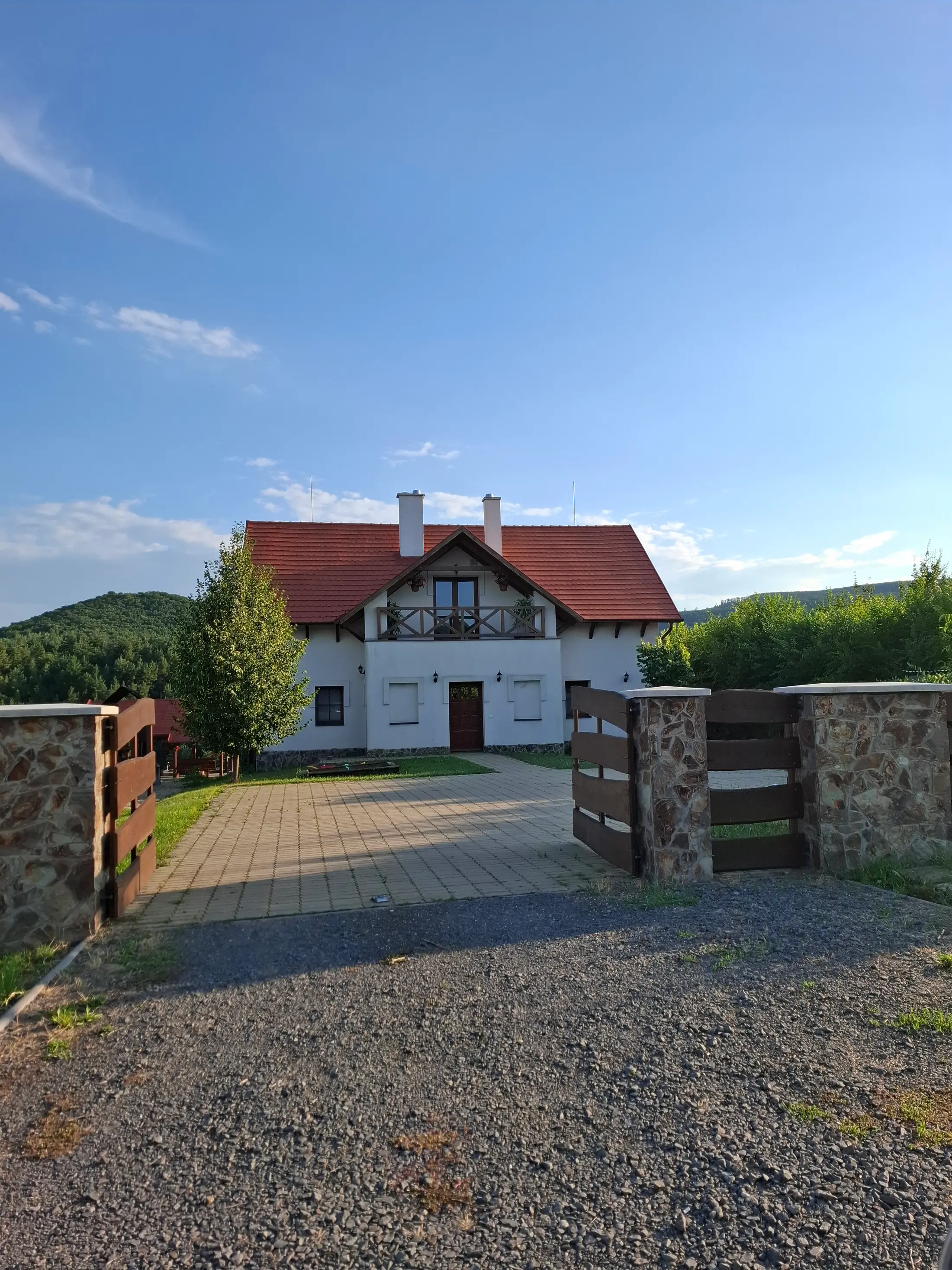 A vendégház homlokzata nappali fényben, előtérben a kerttel